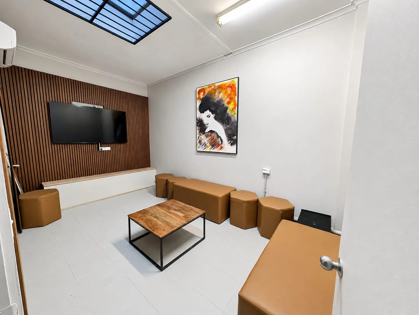 Karaoke Room — lounge with a wall-mounted TV, timber panelling and tan ottoman seating